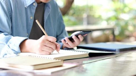 Online study, Student man hand writing on notebook while using mobile phone f Stock Photos