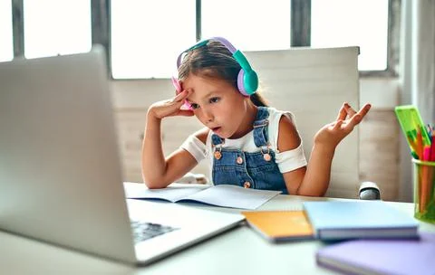 Online training. Child girl in headphones listens to a lesson on a laptop. Sc Stock Photos