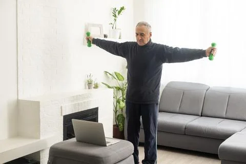 Online workout. elderly man doing exercise with online tutorial at home 库存照片