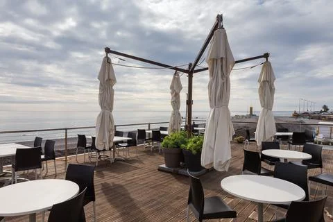 Open area of empty coastal cafe with folded outdoor umbrellas Фото