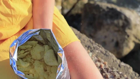 Open bag of crispy potato chips in sunlight on rocky seaside background Stock Footage 317082193