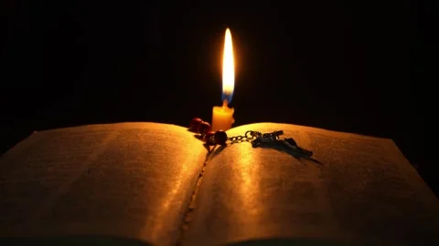An open Bible in the dark in the light of a burning candle. Rosary on a book Stock Footage 274026490