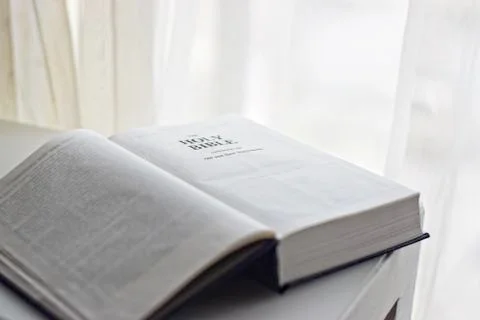 Open bible next to the window on the first page Stock Photos