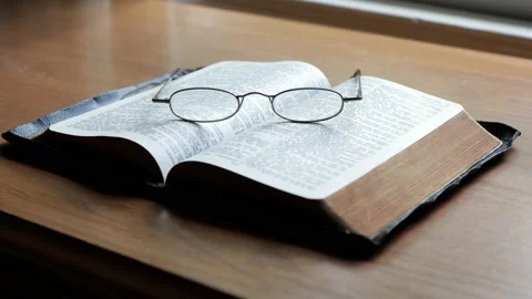 Open bible with reading glasses on a desk Stock Footage 138510364