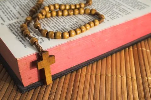 Open Bible with rosaries-beads crucifix on a straw table Stock Photos