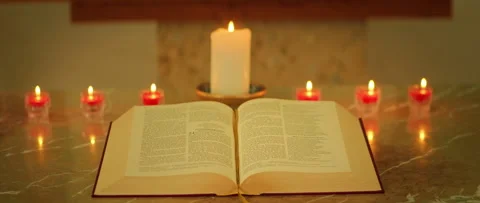 Open Bible surrounded by lit red votive candles and large white candle in church Video stock 313705501