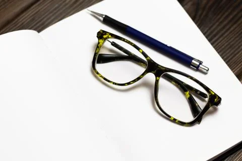 Open blank notebook with a pen and modern black green glasses on dark wooden  Stock Photos