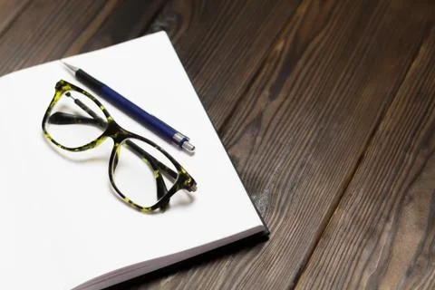 Open blank notebook with a pen and modern black green glasses on dark wooden  Stock Photos