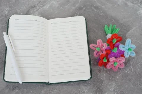 Open blank notebook with pen placed on marble background next to colorful handma Stock-Fotos