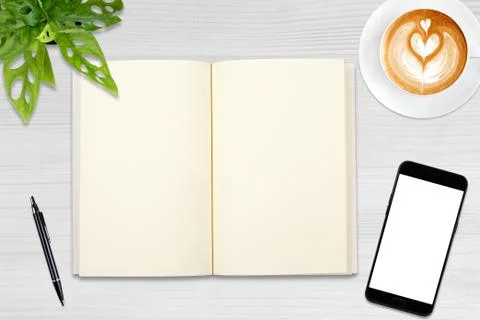 An open blank notebook, smartphone with pen and a cup of latte coffee on wood 写真素材