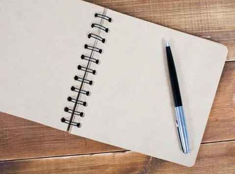 An open blank square notebook of brown kraft paper with a spiral and a ballpo Stock Photos