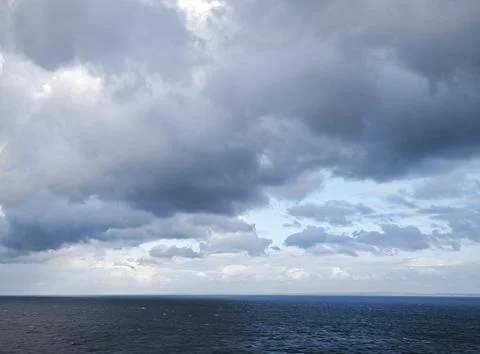 Open Blue Sea Under Dramatic Cloud Formation with Sunlight Illuminating the Ocea Stock Photos