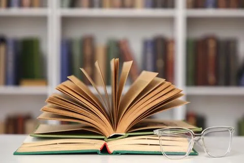 Open book and eyeglasses on table in stylish home library, closeup Fotos de archivo