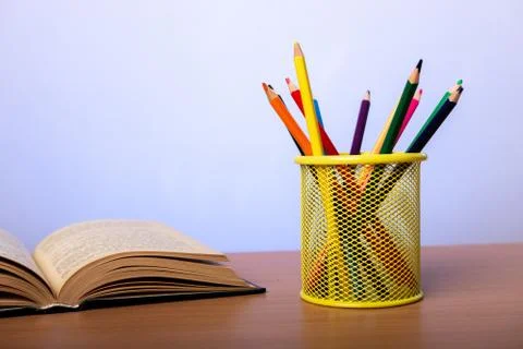 An open book and a jar with multi-colored pencils lie on a table Stock Photos