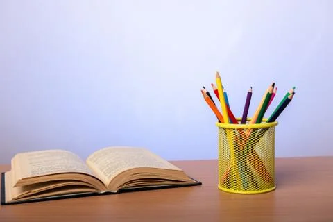 Open book and a jar with multi-colored pencils on a table Stock Photos