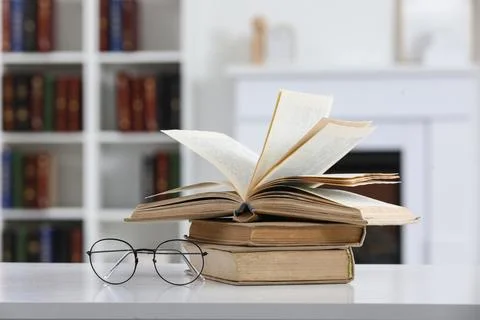 Open book and stack of old books with eyeglasses on white table, library back Stock Photos