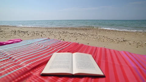 Open Book on Beach Mat Amidst Splashing Waves Stock Footage 250474382