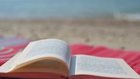 Open Book on Beach Mat with Waves and wind blows the pages Stock Footage 250473992