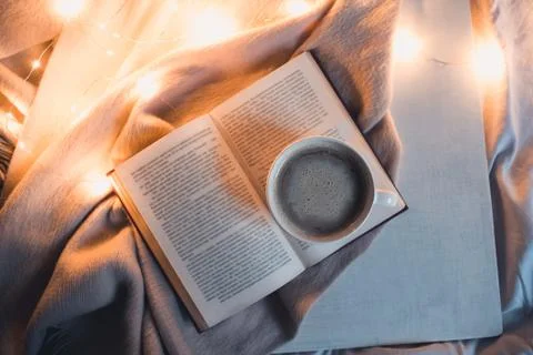 Open book with cup of coffee in bed at night. Top view. Stock Photos