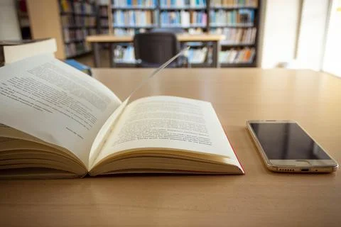 Open book in the library with cell phone on the table Stock Photos