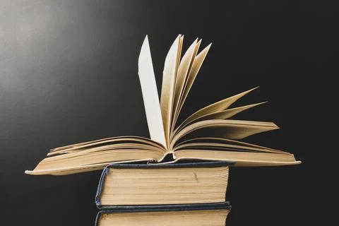An open book lies on a stack of books on a black background. Education. Back Stock Photos