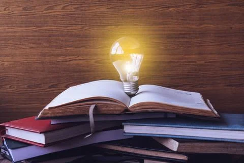 Open book with light bulb and hardback books on wood wall background. Selec.. Stock Photos
