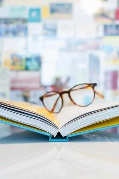 Open book lying on white table with soft blurred reading glasses Stock Photos
