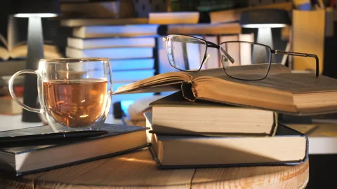 Open book with reading glasses and tea cup on wooden table indoors Stock Footage 336947708