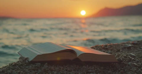 Open book rests on pebbles as sun sets over ocean in serene landscape of Croatia Stock Footage 313016203