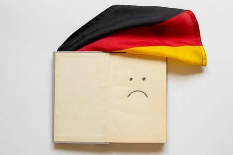 An open book with a sad smiley face drawn on the page and the German flag on  Stock Photos