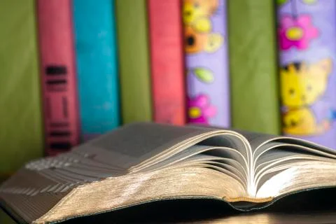 Open book, stack of colorful hardback books on light table. Stock Photos
