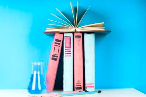 Open book, stack of colorful hardback books on light table. Stock Photos