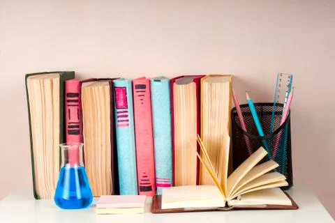 Open book, stack of colorful hardback books on light table. Stock Photos
