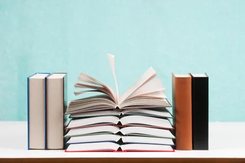 Open book, stack of hardback books on table Stock Photos