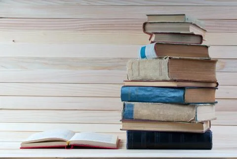 Open book, stack of hardback books on wooden table. Stock Photos