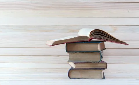 Open book, stack of hardback books on wooden table. Stock Photos