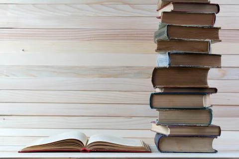 Open book, stack of hardback books on wooden table. Stock Photos