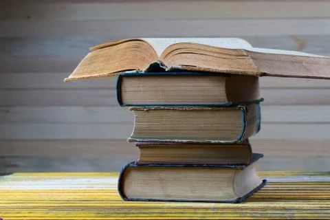 Open book, stack of hardback books on wooden table. Stock Photos