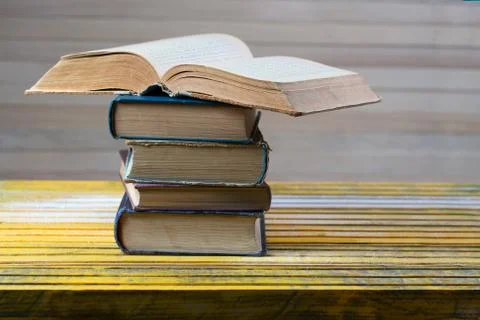 Open book, stack of hardback books on wooden table. Stock Photos