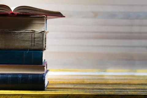 Open book, stack of hardback books on wooden table. Stock Photos