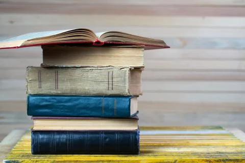 Open book, stack of hardback books on wooden table. Stock Photos