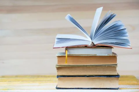 Open book, stack of hardback books on wooden table. Stock Photos