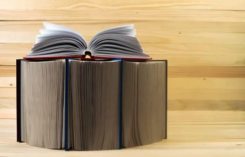 Open book, stack of hardback books on wooden table. Stock Photos