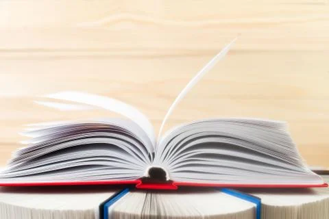 Open book, stack of hardback books on wooden table. Stock Photos