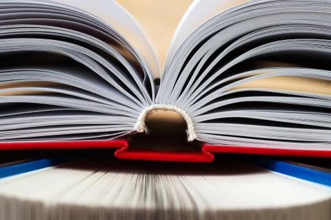 Open book, stack of hardback books on wooden table. Stock Photos