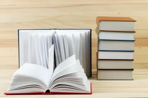 Open book, stack of hardback books on wooden table Stock Photos