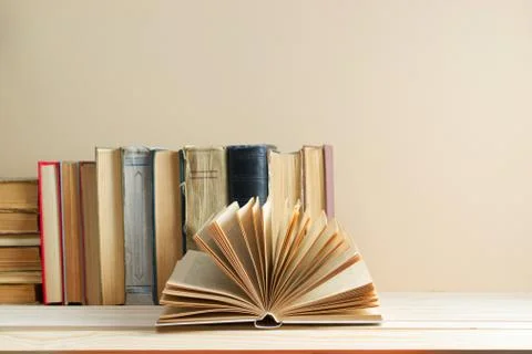 Open book, stack of hardback books on table. Stock Photos