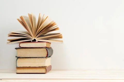 Open book, stack of hardback books on table. Stock Photos