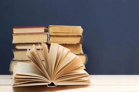 Open book, stack of hardback books on wooden table Stock Photos