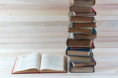 Open book, stack of hardback books on wooden table. Stock Photos